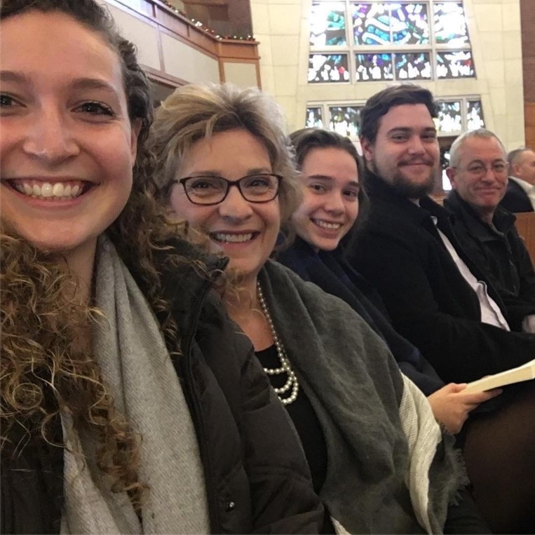 Ms. Schauss smiling and sitting with other people in a church. 